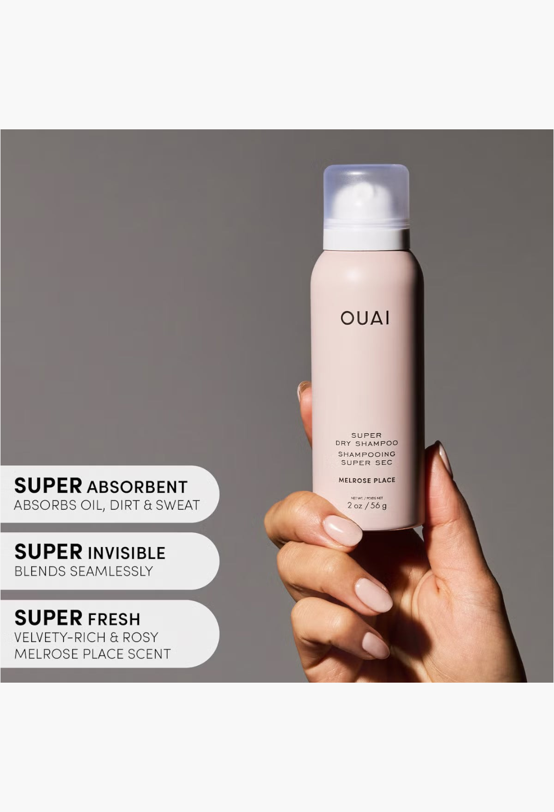 GLAM MODA OUAI Super Dry Shampoo in a travel-sized pale pink aerosol bottle held by a hand against a white background.