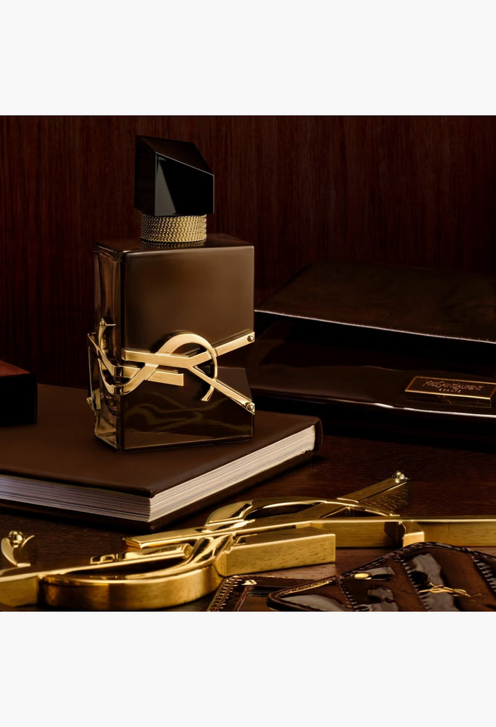 GLAM MODA YSL Libre Santal Couture perfume bottle in chocolate brown glass with gold logo on a dark wooden desk