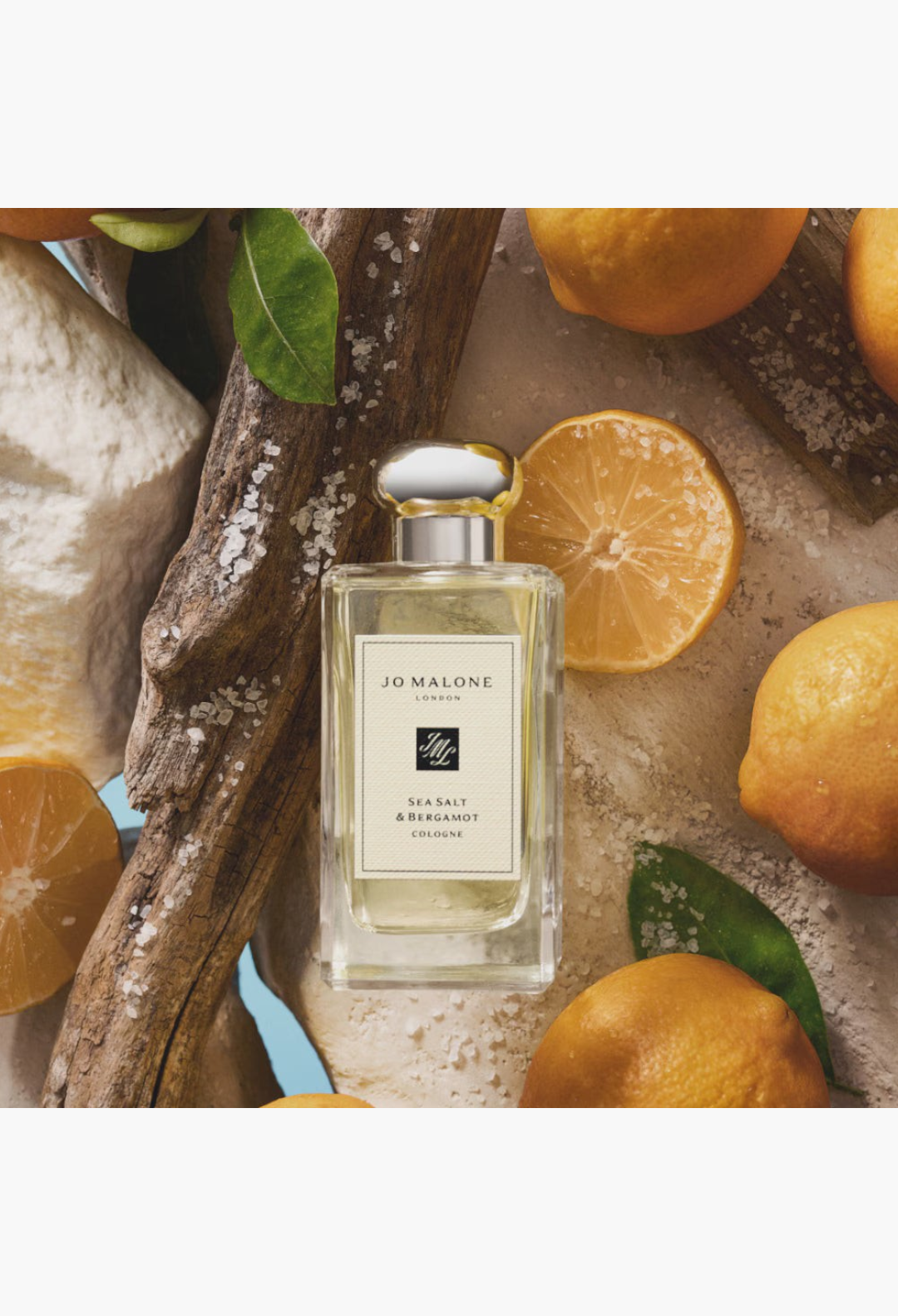 GLAM MODA Sea Salt & Bergamot cologne bottle surrounded by fresh bergamot slices, driftwood, and sea salt crystals.