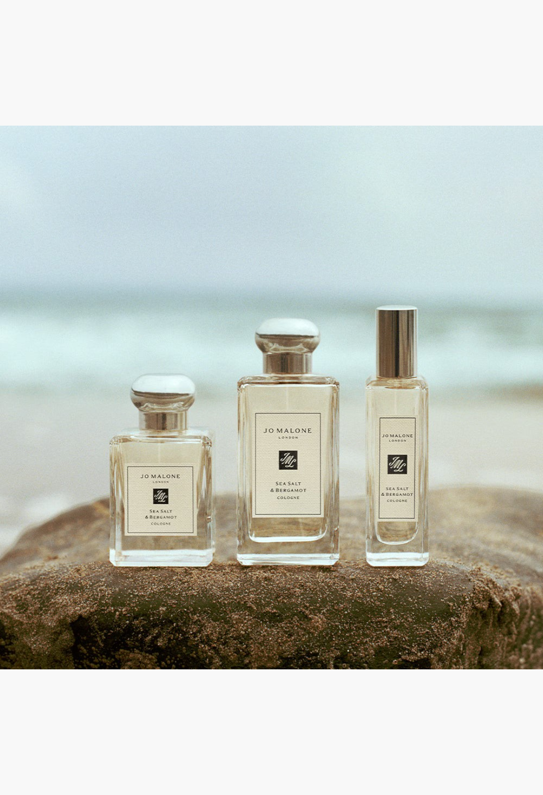 GLAM MODA Sea Salt & Bergamot cologne bottles displayed on a rocky beach with the ocean in the background.