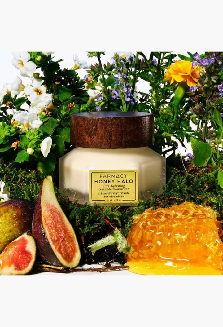 GLAM MODA Honey Halo ceramide moisturizer jar surrounded by fresh figs, honeycomb, and wildflowers on mossy ground.
