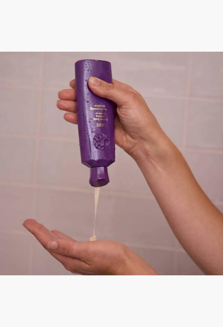 GLAM MODA Serene Scalp densifying conditioner being squeezed from a purple bottle into a hand for thinning hair