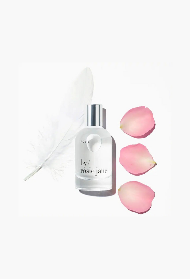 GLAM MODA By Rosie Jane Rosie eau de parfum bottle with a white feather and three pink rose petals on white background