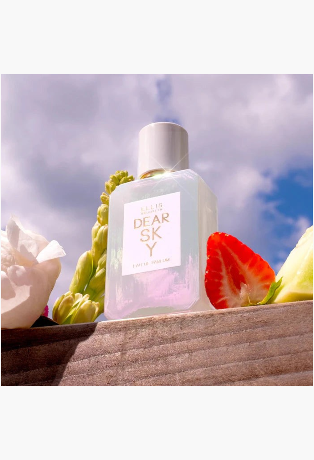 GLAM MODA Ellis Brooklyn Dear Sky perfume bottle surrounded by fresh strawberry slices and white floral petals.