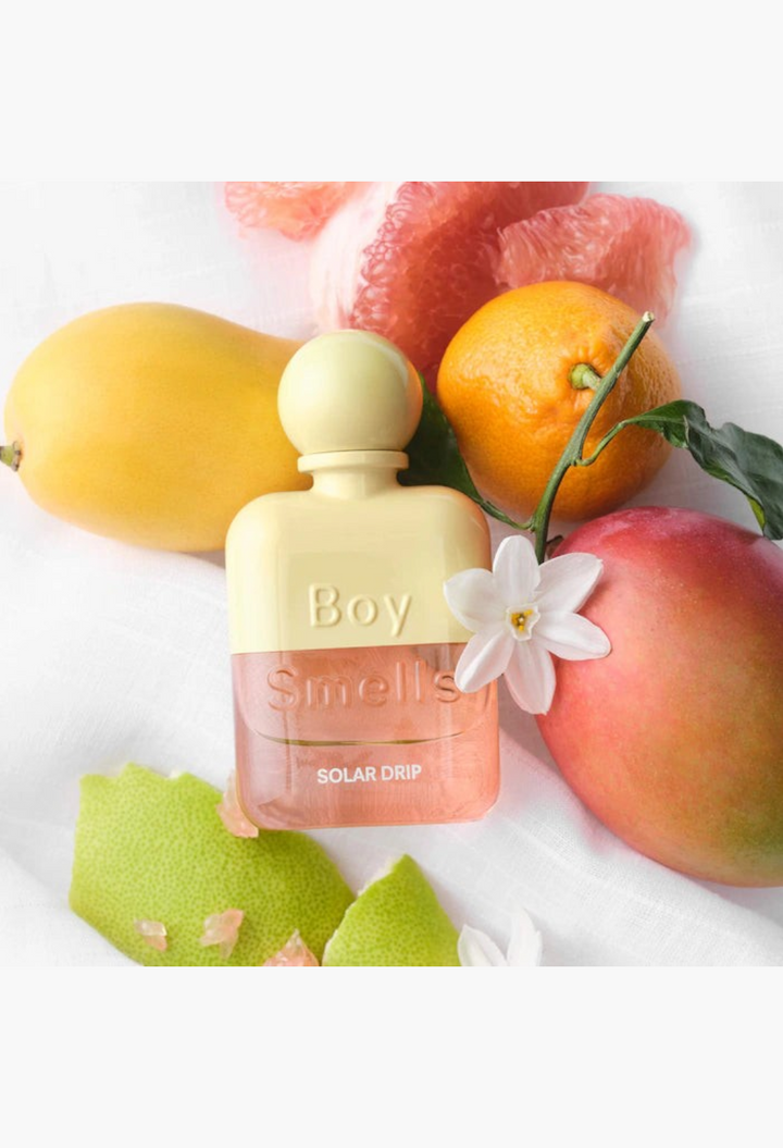 GLAM MODA Solar Drip perfume bottle surrounded by fresh pomelo, mango, and orange blossom flowers