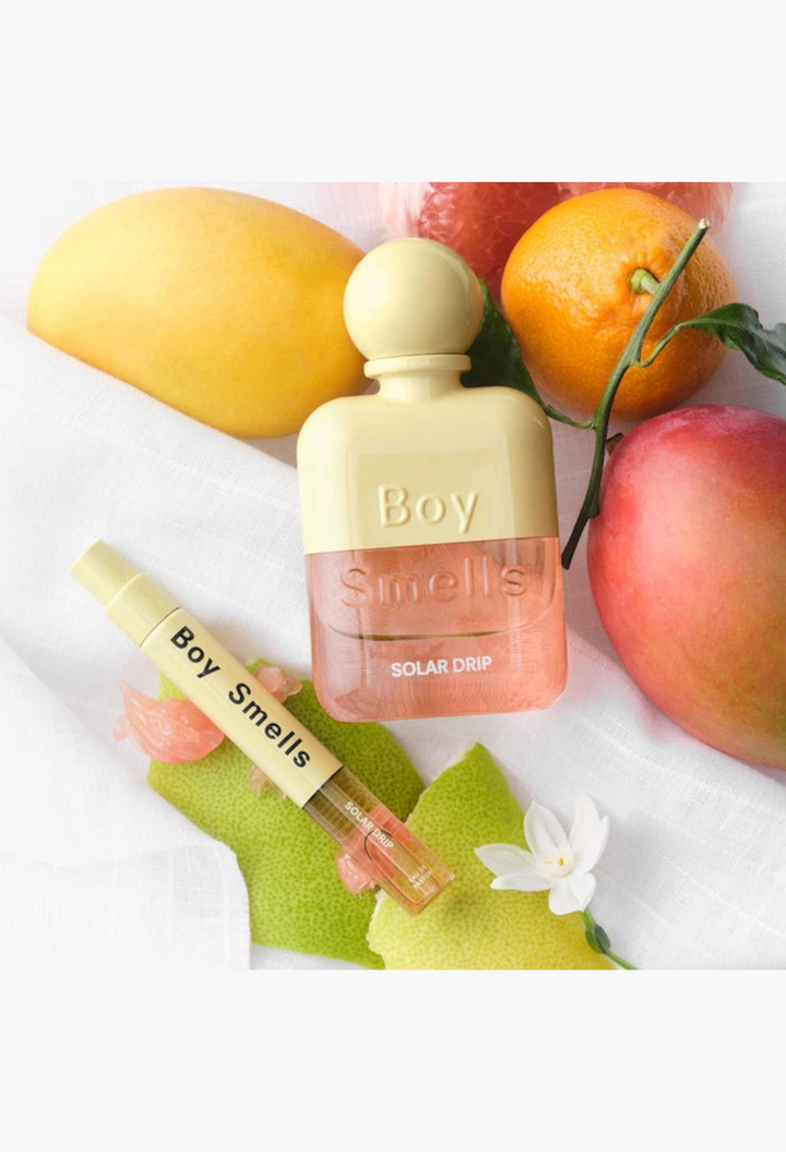 GLAM MODA Solar Drip perfume bottle and travel spray surrounded by fresh mango, orange, and orange blossom flowers.