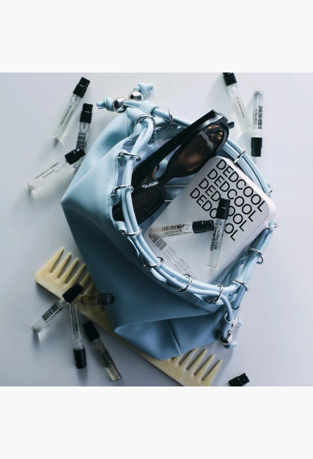 GLAM MODA DedCool fragrance discovery set with six mini vegan perfumes, light blue pouch, sunglasses, and hair comb.