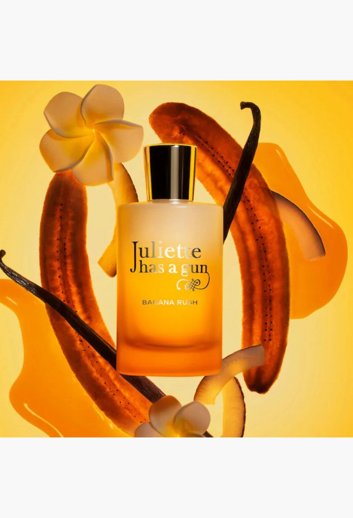 GLAM MODA Juliette Has a Gun Banana Rush perfume bottle surrounded by banana slices, vanilla beans, and white flowers.