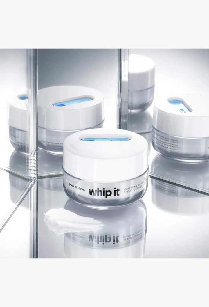 GLAM MODA Whip It hydrating whipped cream jar with blue spatula on a reflective surface for skin barrier support.