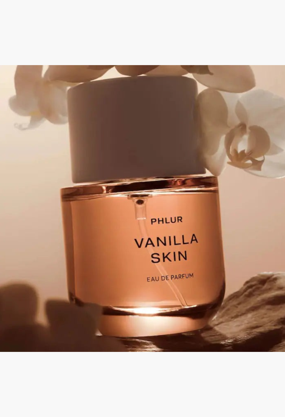 GLAM MODA Phlur Vanilla Skin Eau de Parfum bottle with warm amber liquid, white orchid flowers, and stone base.