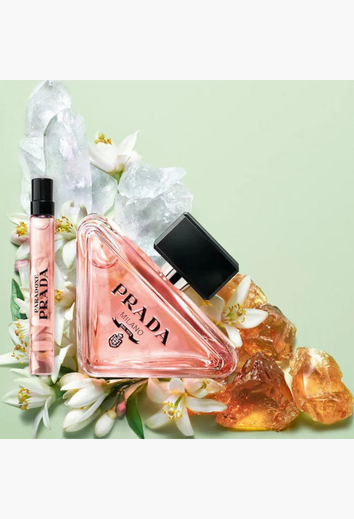GLAM MODA Prada Paradoxe perfume set featuring a triangular glass bottle and sample vial with white flowers and crystals.