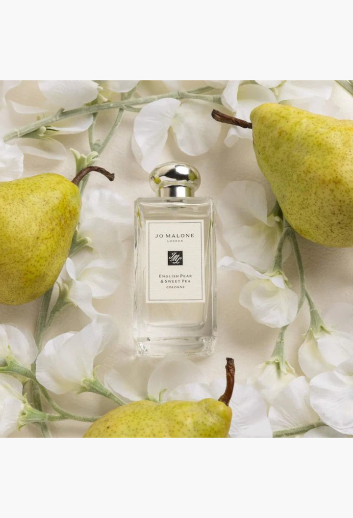 GLAM MODA Jo Malone London English Pear and Sweet Pea cologne bottle surrounded by fresh pears and white flowers.
