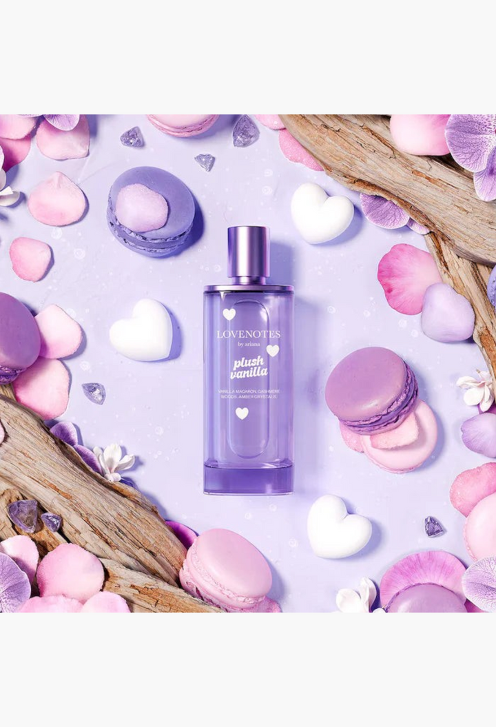 GLAM MODA Ariana Grande Lovenotes Plush Vanilla perfume bottle surrounded by purple macarons, flower petals, and hearts.